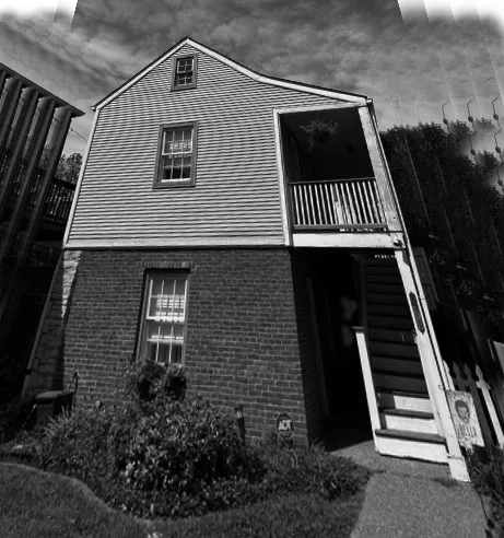 A small brick and frame house with an exterior stair, in black and white.