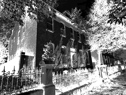 A brick house behind an iron fence in high-contrast black and white.